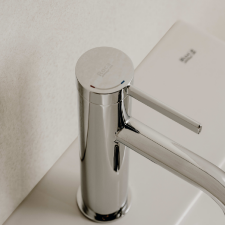 Close-up of a shiny chrome faucet with a horizontal lever, mounted on a white sink against a light wall.