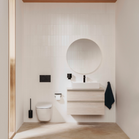 Minimalist bathroom with a wall-mounted toilet, circular mirror, and floating wooden vanity with sink; black fixtures and a towel hanging on the right. White tiled walls and beige floor.