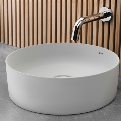 White circular freestanding sink with a chrome faucet mounted on a wooden slat wall, showing the Roca logo inside the bowl.