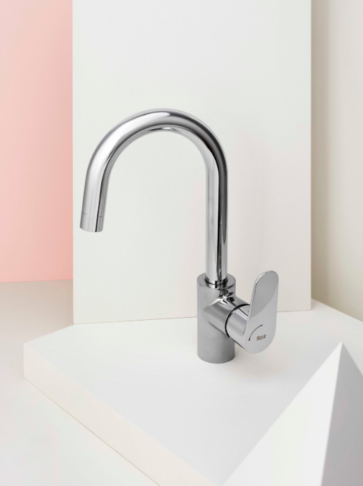 Екранна снимка 2026-07-31 104523 - Мебели за баня и душкабини Polished chrome faucet with a high curved spout and single lever, mounted on a white pedestal against a pale pink backdrop (modern fixture).