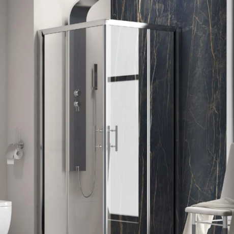 Frameless glass shower enclosure with a chrome frame in a modern bathroom with dark marble walls behind it.