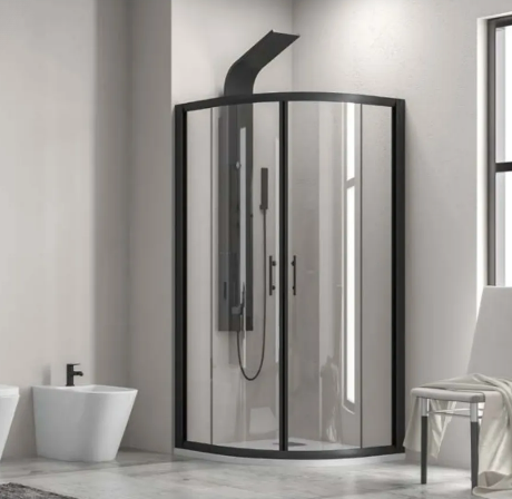 Modern bathroom with a curved glass shower enclosure and black frame in the corner; a bidet and toilet are on the left, while a chair with a towel sits by a window on the right.
