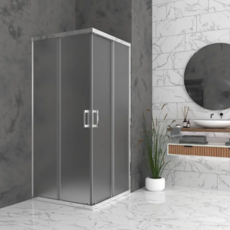 Modern bathroom featuring a gray-framed glass shower enclosure, white marble floors, and a round mirror above a floating vanity; a tall plant in a white pot sits by the shower.