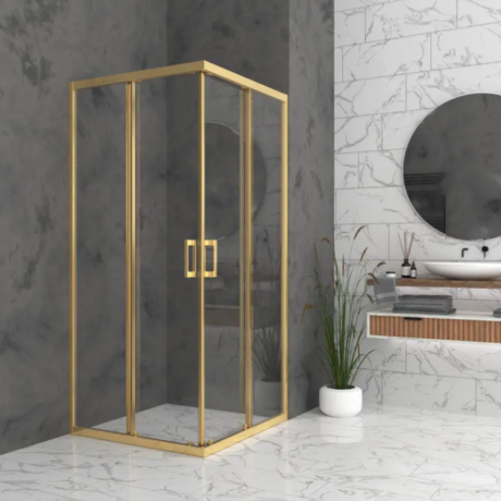 Gold-framed glass shower enclosure in a marble bathroom with a round mirror and a potted plant nearby