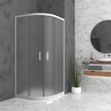 Curved glass shower enclosure in a modern marble bathroom with a round mirror and potted plant nearby.