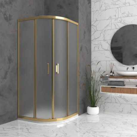 Curved glass shower enclosure with a gold frame in a marble-tinished bathroom, paired with a round mirror and white vessel sink.