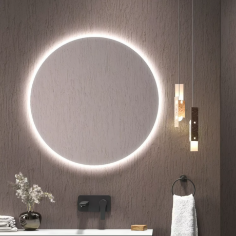Round backlit mirror on a textured wall with a modern black faucet, towel ring, and white towel to the right; decorative vase with flowers on a counter.