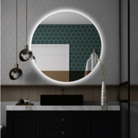 Round backlit mirror above a marble-topped bathroom vanity with a black sink, dark cabinetry, hexagonal wall tiles, bronze pendant lights, and a vase on the counter.