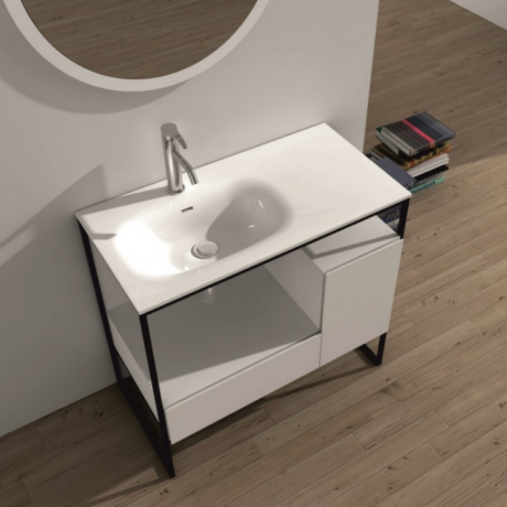 Modern white bathroom sink on a metal-framed vanity with a round mirror above and a stack of books on the floor to the right.