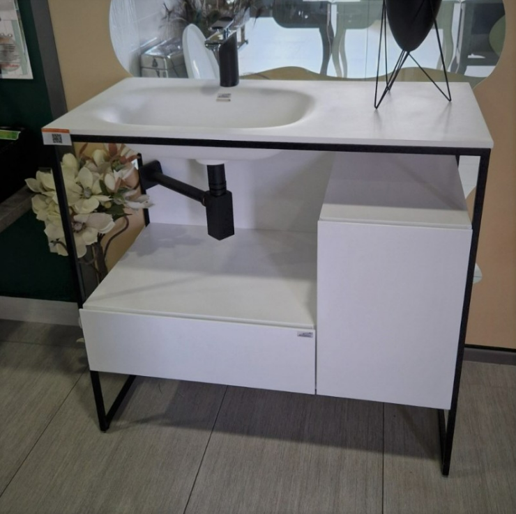 Екранна снимка 2026-08-04 075636 - Мебели за баня и душкабини White bathroom vanity with open shelf and metal frame, under-mounted sink, and exposed plumbing pipe visible beneath the sink.