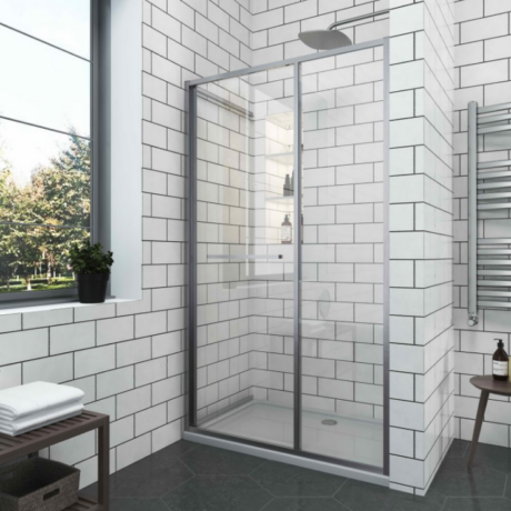 Glass-framed shower enclosure with sliding doors in a modern bathroom, white subway-tiled walls, and a rainfall showerhead near a windowled wall.