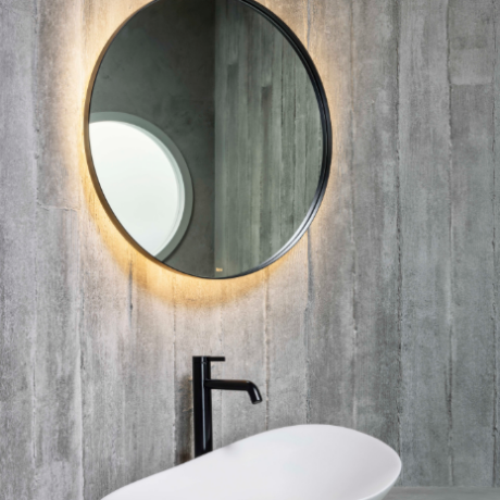 Circular backlit mirror above a white oval vessel sink with a black faucet on a gray concrete vanity; soap bar on the counter