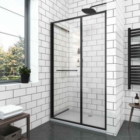 Modern bathroom shower with two-panel glass doors and a black metal frame, surrounded by white subway tiles, near a window with a plant.”] ,