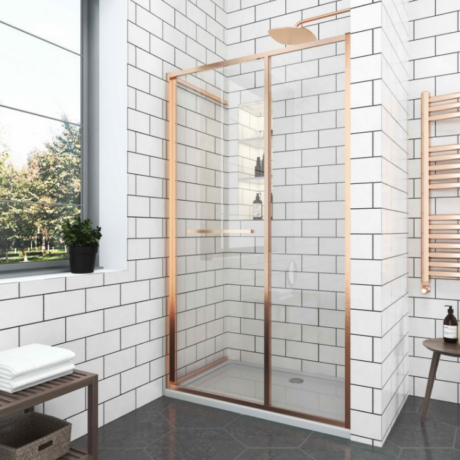 Modern bathroom with a rose-gold framed glass shower enclosure, white subway-tile walls, and a window with a plant on the sill.